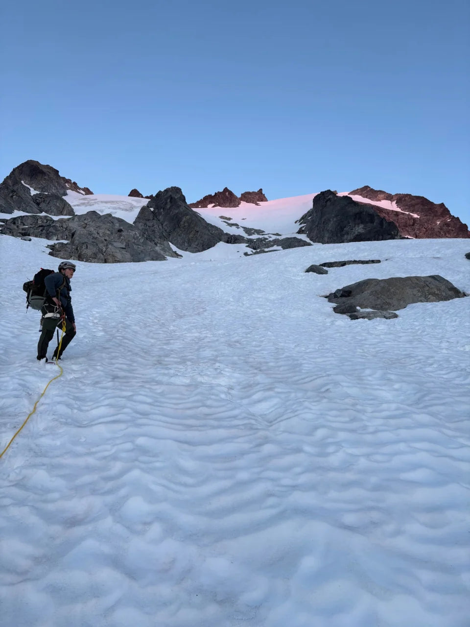 Oscar ascending a snow slope toward rocks in the evening light.