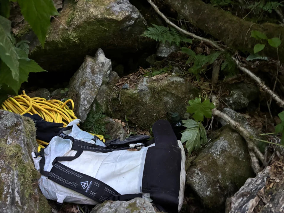 A backpack and climbing rope between moss-covered rocks beside flowing water.