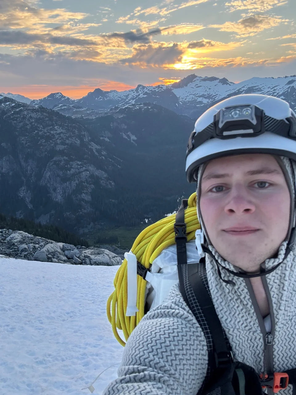 Rowan in a climbing helmet with sunset above the mountain range.